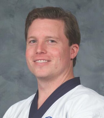 A smiling individual in a martial arts uniform, facing the camera with a neutral background.
