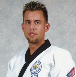 A martial arts practitioner wearing a white gi, smiling confidently for the camera, with styled hair and a black belt.