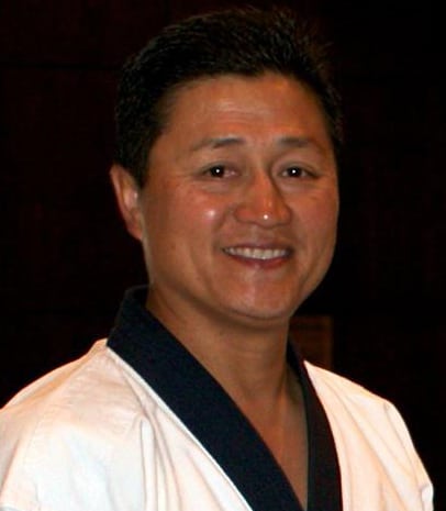 A smiling martial arts practitioner wearing a traditional uniform, expressing confidence and warmth, captured in a close-up portrait.