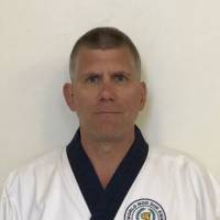 A serious-looking person wearing a martial arts uniform with a dark collar, set against a plain background.